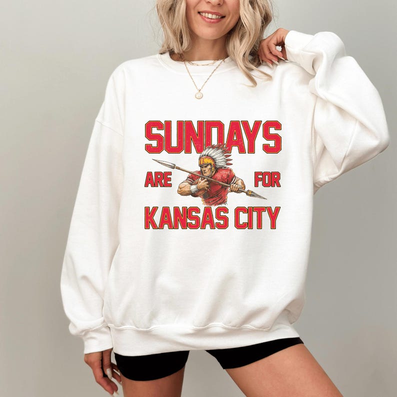 A woman wearing a white sweatshirt with a graphic design that says "SUNDAYS ARE FOR KANSAS CITY" and features an illustration of a Native American warrior.