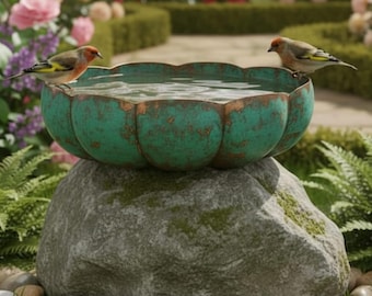 May include: A weathered, turquoise bird bath with a scalloped edge, filled with water, sits atop a large, moss-covered rock. Two small birds perch on the edge. The background features a garden with flowers and a pathway.