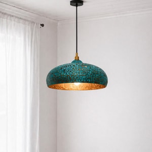 Może przedstawiać: Turkusowa i złota lampa wisząca. Klosz w kształcie kopuły ma teksturowany, młotkowany wygląd z turkusowym zewnętrzem i złotym wnętrzem. Światło zwisa z czarnego przewodu i złotego mocowania.