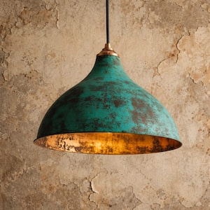 May include: A teal-colored pendant light with a copper-colored interior. The light fixture has a dome shape and a distressed finish, hanging from a black cord. The ceiling fixture is a decorative element for home decor.