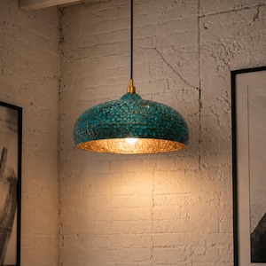 May include: A teal and gold pendant light fixture. The dome-shaped shade has a textured surface with a teal finish on the outside and a gold interior. The light hangs from a black cord with a brass-colored fixture.