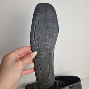 May include: Black leather loafers with a rubber sole. The sole is textured with a pattern of grooves and the brand name "TOD'S" is visible. The shoe is held up to show the sole.