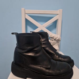 May include: Black leather ankle boots with a zip front and a chunky sole. The boots have a rounded toe and a smooth finish. The boots are approximately 15 cm in height.