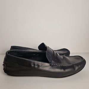 May include: A pair of black leather loafers. The shoes have a classic design with a rounded toe, a penny strap, and a rubber sole. The loafers are made of smooth, high-quality leather.