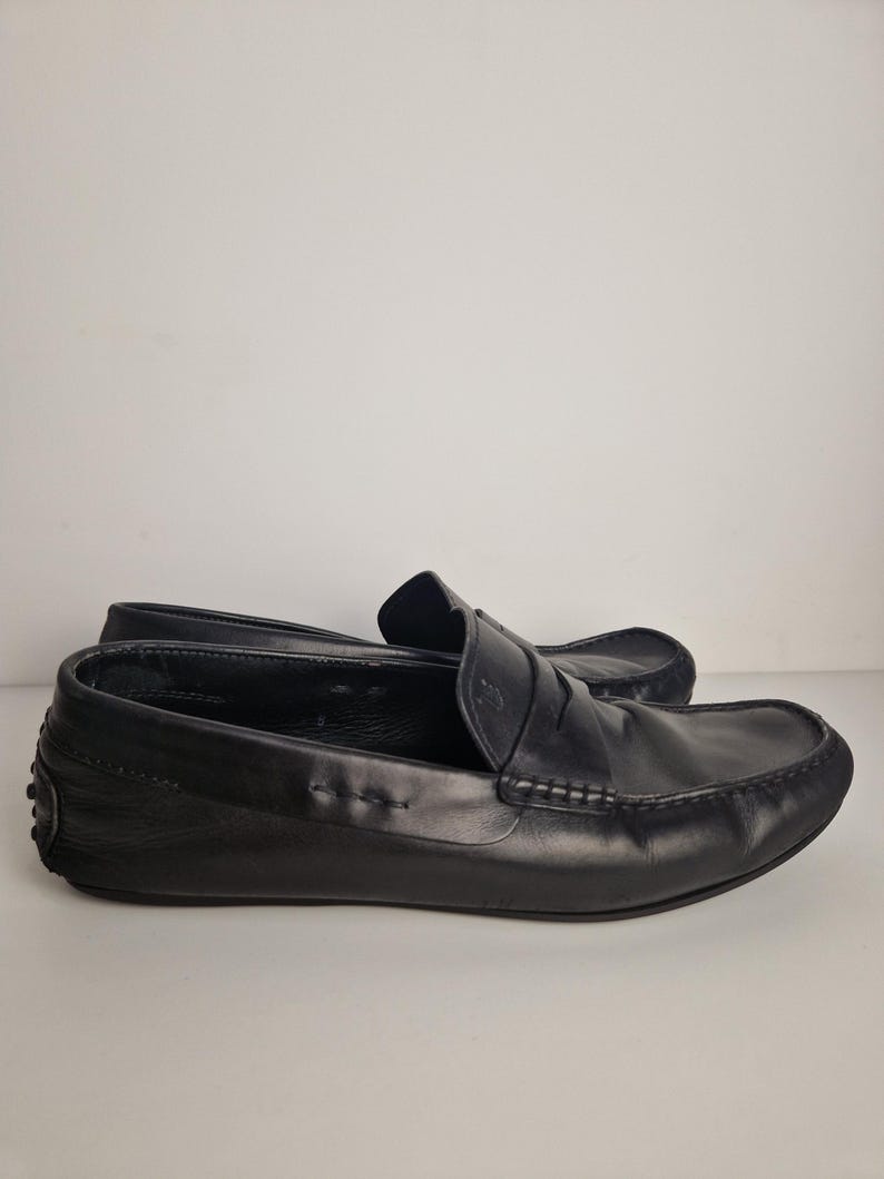May include: A pair of black leather loafers. The shoes have a classic design with a rounded toe, a penny strap, and a rubber sole. The loafers are made of smooth, high-quality leather.