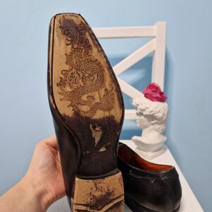 Puede incluir: Zapatos de vestir de cuero negro con un dise&ntilde;o de drag&oacute;n detallado tallado en la suela. Los zapatos tienen un dise&ntilde;o cl&aacute;sico con un tac&oacute;n bajo y un acabado liso. El forro interior es naranja.