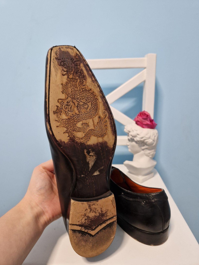 Puede incluir: Zapatos de vestir de cuero negro con un dise&ntilde;o de drag&oacute;n detallado tallado en la suela. Los zapatos tienen un dise&ntilde;o cl&aacute;sico con un tac&oacute;n bajo y un acabado liso. El forro interior es naranja.