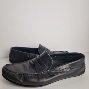 May include: A pair of black leather loafers. The shoes have a classic design with a rounded toe, a strap across the vamp, and a rubber sole. The leather appears to be slightly distressed, giving the shoes a worn-in look.
