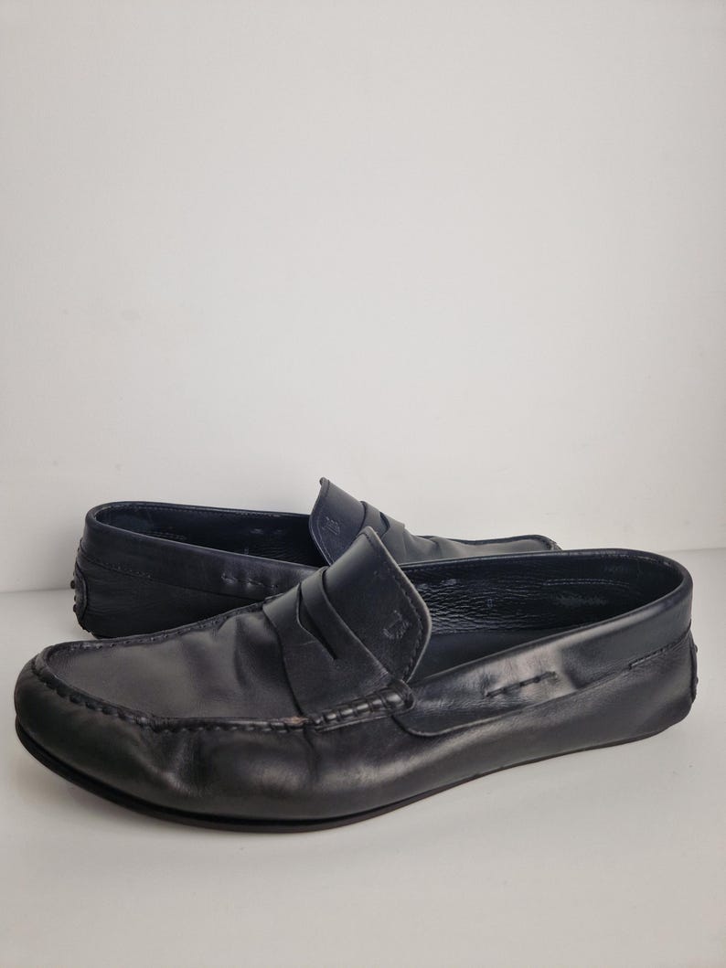 May include: A pair of black leather loafers. The shoes have a classic design with a rounded toe, a strap across the vamp, and a rubber sole. The leather appears to be slightly distressed, giving the shoes a worn-in look.