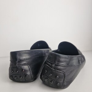 May include: Close-up of two black leather loafers. The shoes have a classic design with a rounded toe and a rubber sole with small, round studs. The leather appears to be smooth and slightly worn, giving the shoes a vintage look.