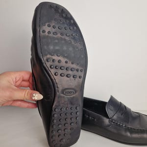 May include: Black leather loafers with a rubber sole featuring a pattern of small circles. The sole shows wear. The loafers have a classic design with a stitched vamp and a penny keeper strap.