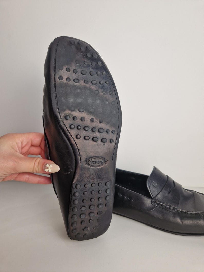 May include: Black leather loafers with a rubber sole featuring a pattern of small circles. The sole shows wear. The loafers have a classic design with a stitched vamp and a penny keeper strap.