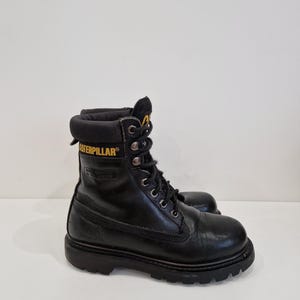 Puede incluir: Una taza de cer&aacute;mica blanca con un asa negra y el texto "But First, Coffee" en negro, en negrita. La taza est&aacute; sobre una superficie blanca.