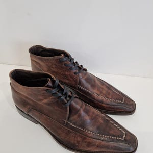 May include: A pair of brown leather ankle boots with black laces. The boots have a pointed toe design with decorative stitching. The leather has a distressed appearance, adding to the vintage aesthetic. The boots are suitable for various occasions.