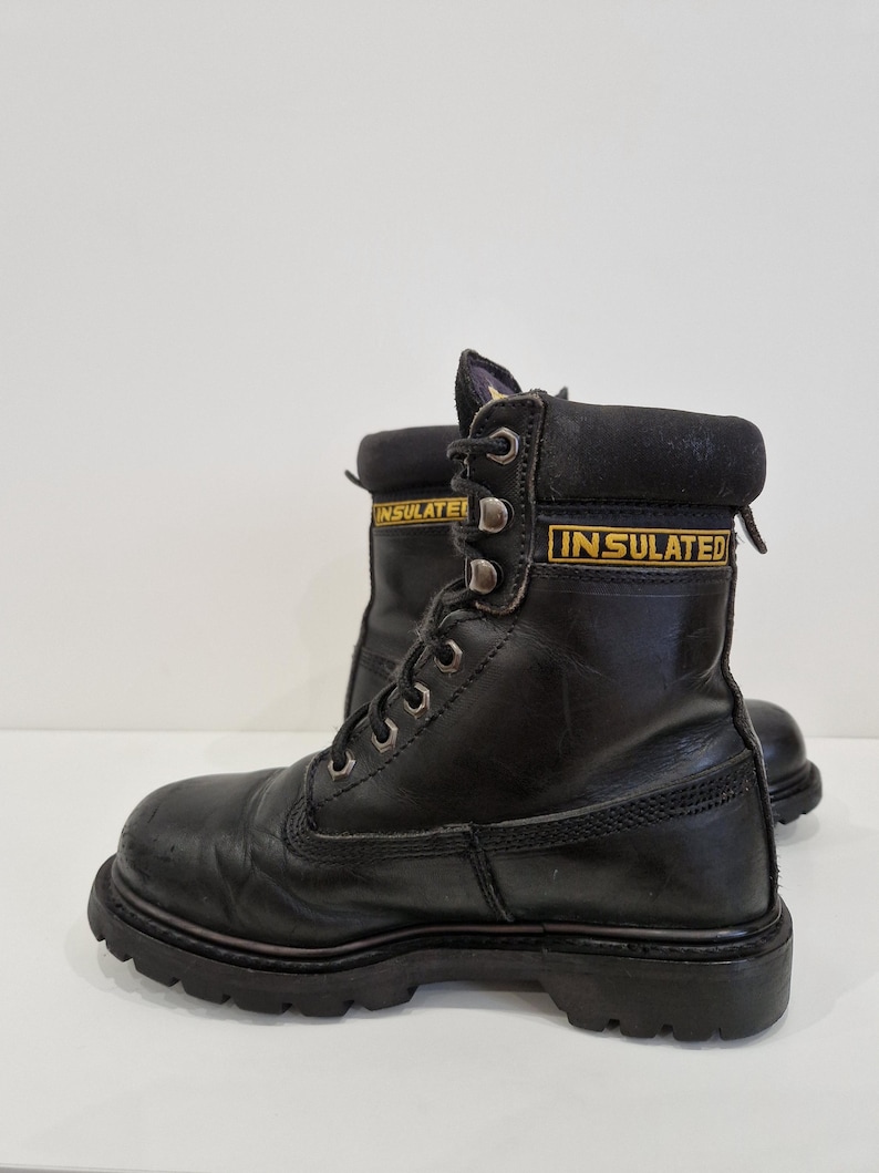 Puede incluir: Par de botas de trabajo de cuero negro con suela resistente. Las botas tienen ojales met&aacute;licos para los cordones y la palabra "INSULATED" en letras amarillas en el cuello. Las botas est&aacute;n dise&ntilde;adas para la durabilidad y la protecci&oacute;n.