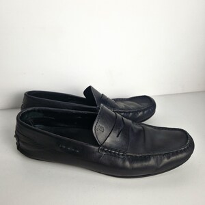 May include: A pair of black leather loafers. The shoes have a classic design with a rounded toe, a penny strap, and a stitched sole. The leather appears to be smooth and slightly worn. The loafers are set against a plain white background.