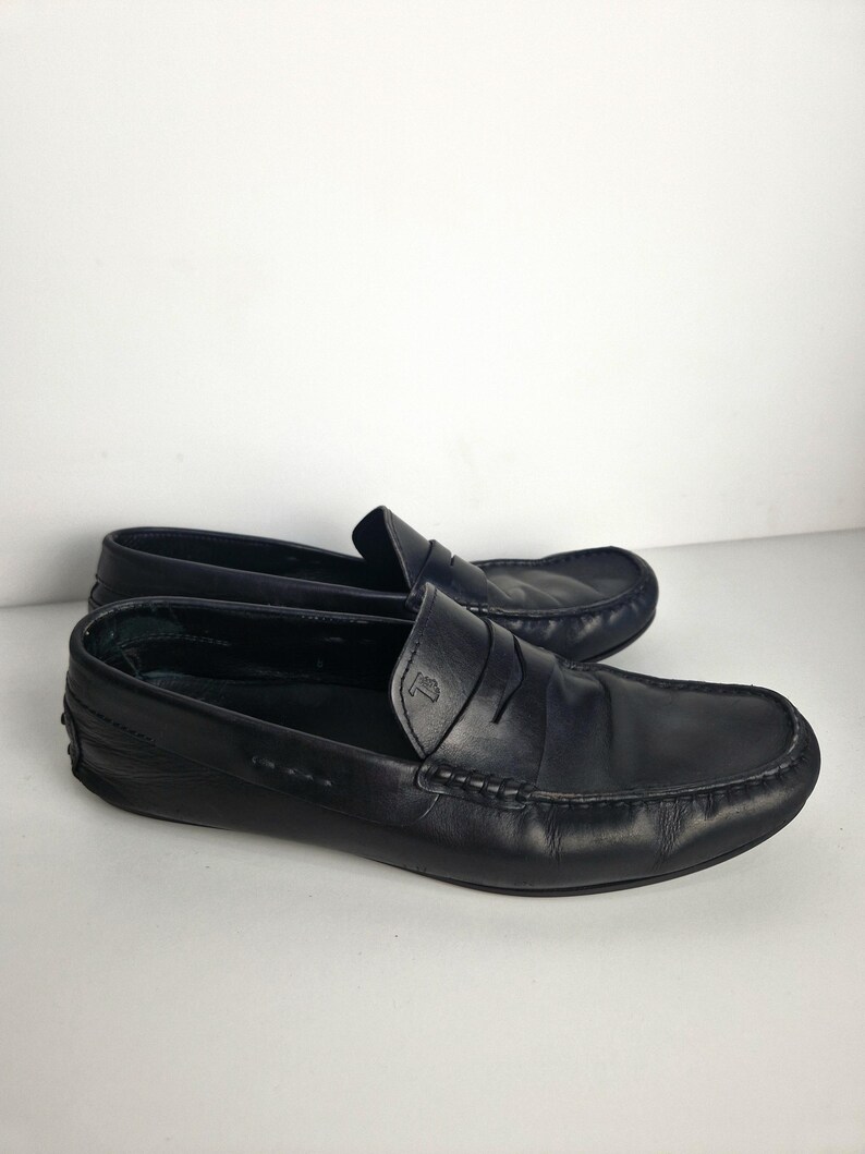 May include: A pair of black leather loafers. The shoes have a classic design with a rounded toe, a penny strap, and a stitched sole. The leather appears to be smooth and slightly worn. The loafers are set against a plain white background.