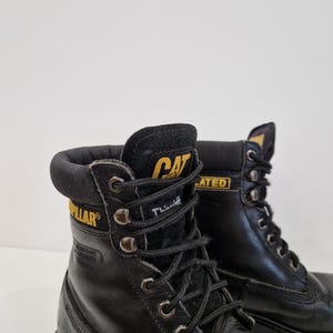 Puede incluir: Botas de trabajo de cuero negro con el logotipo CAT en amarillo. Las botas tienen cordones negros, ojales met&aacute;licos y un cuello acolchado. Las botas est&aacute;n dise&ntilde;adas para el trabajo y tienen una construcci&oacute;n duradera.