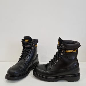 Puede incluir: Una taza de cer&aacute;mica blanca con un asa negra y el texto "But First, Coffee" en negro, con una fuente de estilo manuscrito. La taza est&aacute; sobre una superficie blanca.