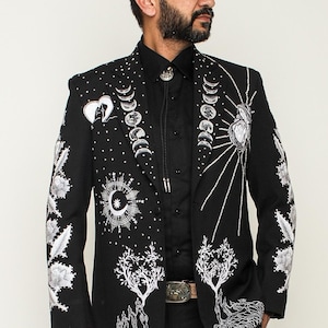May include: A black blazer with silver embroidery of moons, stars, and trees. The blazer is worn with black pants and black shoes.