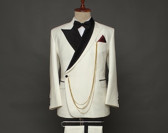 May include: A white tuxedo jacket with a black shawl collar and a gold chain detail. The jacket has a single button closure and a pocket on the left side. The pants are white with a black stripe down the side.