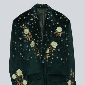 Puede incluir: Una blazer de terciopelo verde oscuro con bordados de rosas blancas y hojas doradas. La blazer presenta un cierre de un solo bot&oacute;n, dos bolsillos delanteros y est&aacute; adornada con adornos en forma de estrella.