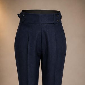 May include: Dark navy blue trousers featuring a high-waisted design with side adjusters, button closures, and a clean, tailored silhouette. These pants include front pleats, a structured waistband, and finished cuffs at the bottom of each leg.