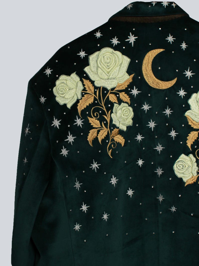 Puede incluir: Chaqueta de terciopelo verde oscuro con rosas crema bordadas, hojas doradas, una luna creciente dorada y detalles de estrellas plateadas. La chaqueta tiene un dise&ntilde;o cl&aacute;sico y a medida, ideal para a&ntilde;adir un toque de elegancia celestial.