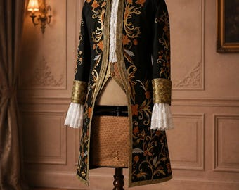 May include: A black long coat featuring intricate gold and orange floral embroidery, a high collar, and wide cuffs. The coat is worn over a white ruffled shirt and a textured tan vest, displayed on a wooden mannequin stand.