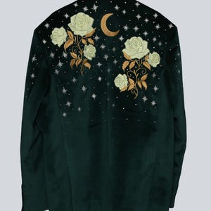 Puede incluir: Una blazer de terciopelo verde oscuro con un dise&ntilde;o celestial bordado. La parte trasera presenta rosas blancas, tallos dorados, una luna creciente dorada y estrellas plateadas. La blazer tiene un corte cl&aacute;sico.