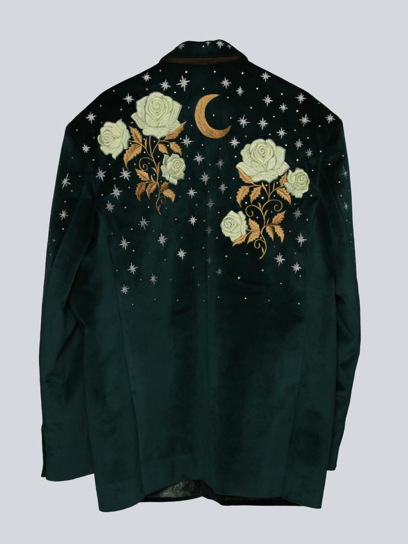 Puede incluir: Blazer de terciopelo verde oscuro con rosas blancas bordadas, tallos dorados, una luna creciente dorada y detalles de estrellas plateadas. La chaqueta tiene un dise&ntilde;o cl&aacute;sico y a medida, ideal para a&ntilde;adir un toque de elegancia celestial a cualquier atuendo.