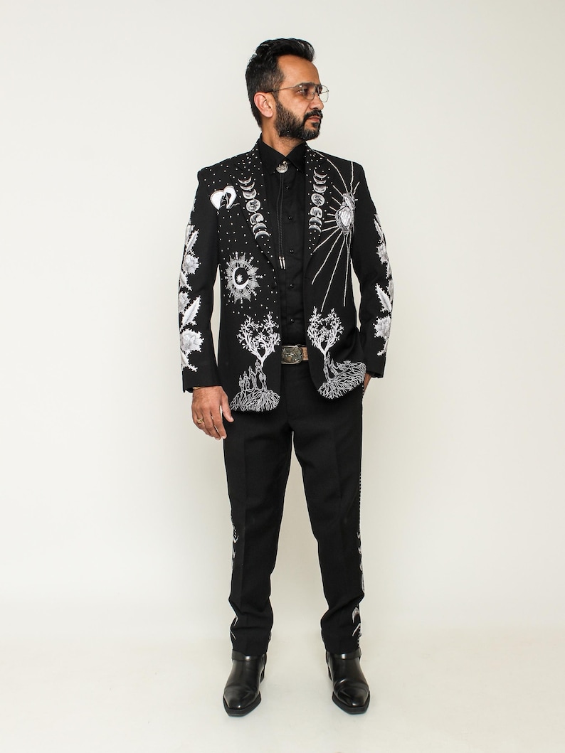 May include: A black blazer with silver embroidery of moons, stars, and trees. The blazer is worn with black pants and black shoes.