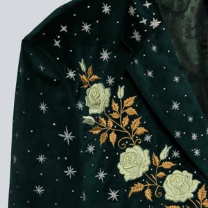 Puede incluir: Blazer de terciopelo verde oscuro con rosas blancas bordadas y hojas doradas. El blazer est&aacute; adornado con estrellas y puntos plateados. El forro interior presenta un estampado de cachemira.