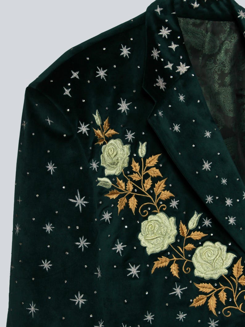 Puede incluir: Blazer de terciopelo verde oscuro con rosas blancas bordadas y hojas doradas. El blazer est&aacute; adornado con estrellas y puntos plateados. El forro interior presenta un estampado de cachemira.