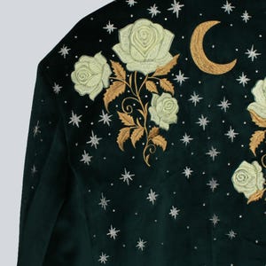 Puede incluir: Chaqueta de terciopelo verde oscuro con rosas crema bordadas, hojas doradas, una luna creciente dorada y detalles de estrellas plateadas. La chaqueta tiene un dise&ntilde;o cl&aacute;sico y a medida, ideal para a&ntilde;adir un toque de elegancia celestial.