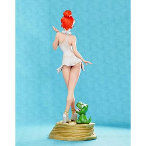 May include: A red-haired figurine of a woman wearing a white dress and standing on a brown base. A small green dinosaur figurine is beside her.