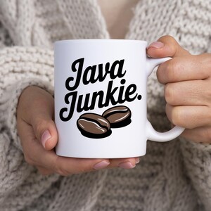 May include: White ceramic mug with black text that reads "Java Junkie." Two brown coffee beans are depicted below the text.
