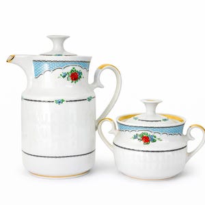 Könnte beinhalten: Ein weißes Keramik-Teeservice mit einer hohen Kanne und einer Zuckerdose mit Deckel. Das Set ist mit blauen Punkten, floralen Akzenten und goldenen Verzierungen verziert. Die Kanne hat einen gebogenen Griff und Ausguss.