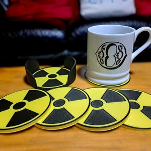 Può includere: Sei sottobicchieri circolari gialli e neri con un design a simbolo di radiazione. Una tazza bianca con un design nero è appoggiata su un sottobicchiere.