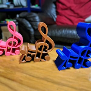Peut inclure: Trois porte-notes de musique en forme de clé de sol imprimés en 3D en rose, marron et bleu.