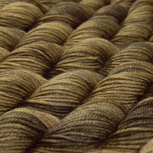 May include: Multiple skeins of yarn arranged in a repeating pattern. Each skein features a variegated color palette of dark brown, tan, and muted olive green tones, showcasing the twisted fiber texture and the individual strands of the yarn.
