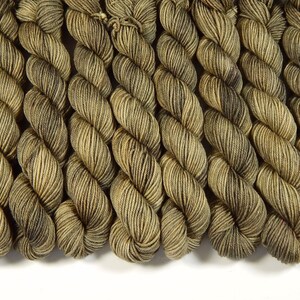 May include: A collection of multiple skeins of yarn arranged in a row. Each skein features a variegated color pattern with shades of olive green, brown, and tan, displaying a twisted, multi-ply texture throughout the length of the fiber.