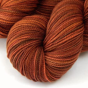 May include: Close-up of a skein of yarn in shades of orange, brown, and rust. The yarn is tightly wound, showing the individual strands and color variations. Ideal for knitting, crocheting, or other fiber arts projects.