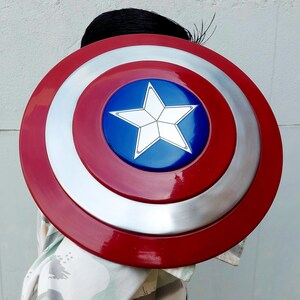May include: A circular shield in red, white, and blue, featuring a star emblem. The shield has a glossy finish. The centre has a blue circle with a white star. The outer ring is red, and the middle ring is silver.