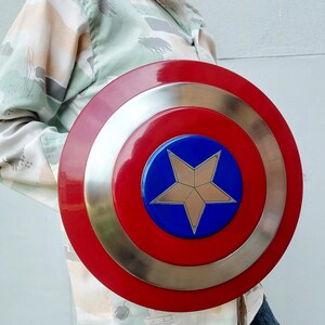 May include: A circular shield featuring a red border, a silver band, and a blue central disc. A gold star is positioned in the middle. This shield is a replica of Captain America's shield.