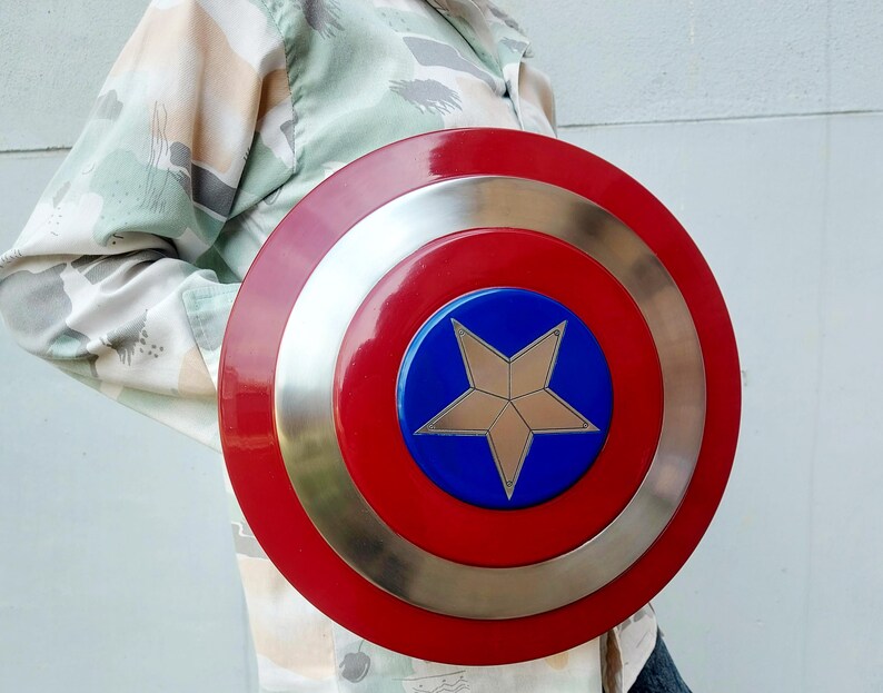 May include: A circular shield featuring a red border, a silver band, and a blue central disc. A gold star is positioned in the middle. This shield is a replica of Captain America's shield.