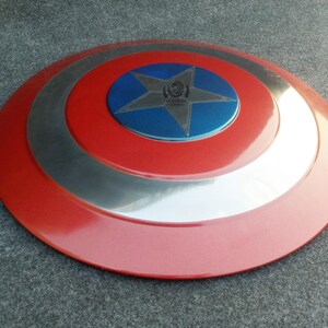 Op de afbeelding: Een rood, wit en blauw Captain America-schild met een vijfpuntige ster in het midden. Het schild heeft een zilveren metalen rand.