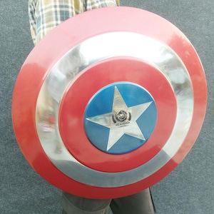 Op de afbeelding: Een rood, wit en blauw Captain America schild met een zilveren ster en het woord "CRANISTA" in het midden. Het schild is gemaakt van metaal en heeft een verhoogde rand.