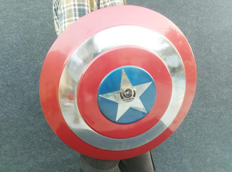 Op de afbeelding: Een rood, wit en blauw Captain America schild met een zilveren ster en het woord "CRANISTA" in het midden. Het schild is gemaakt van metaal en heeft een verhoogde rand.