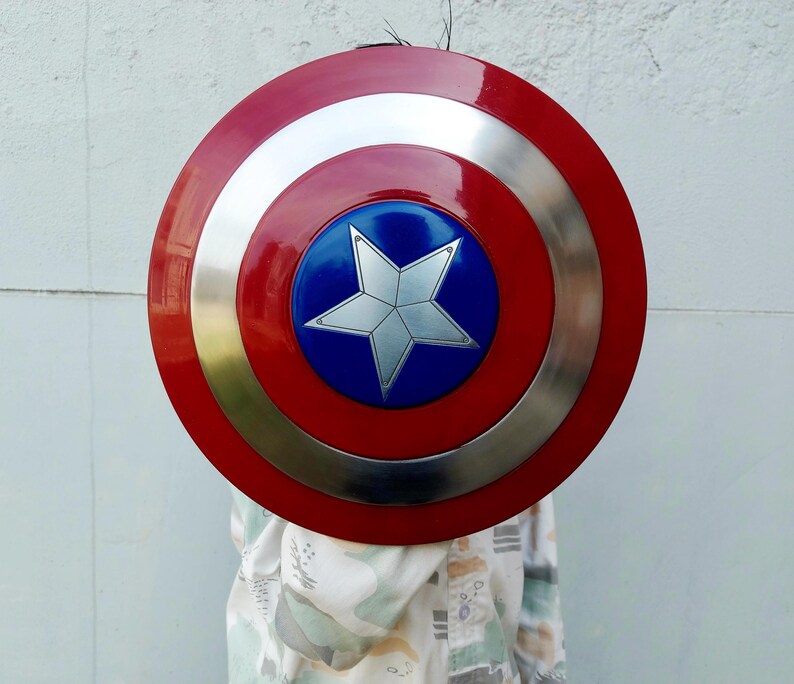 May include: A circular shield in red, silver, and blue. It has a central blue disc with a silver star, encircled by rings of red, silver, and a gold-coloured ring. This shield is a prop.